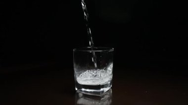 Koyu arkaplanda bardağa sıvı dökülüyor.