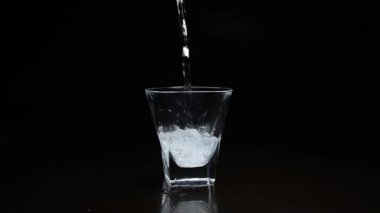 Koyu arkaplanda bardağa sıvı dökülüyor.