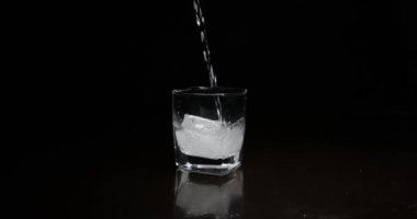 Koyu arkaplanda buzla bardağa alkol dökmek.