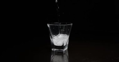 Koyu arkaplanda buzla bardağa alkol dökmek.