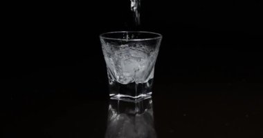 Koyu arkaplanda buzla bardağa alkol dökmek.