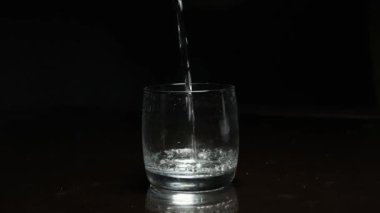 Koyu arkaplanda bardağa sıvı dökülüyor.