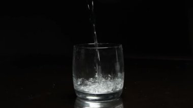 Koyu arkaplanda bardağa sıvı dökülüyor.