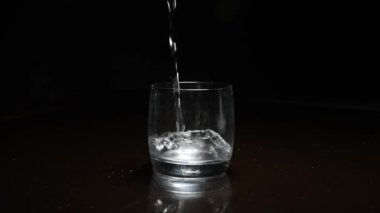 Koyu arkaplanda bardağa sıvı dökülüyor.