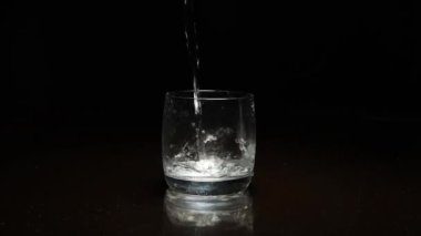 Koyu arkaplanda bardağa sıvı dökülüyor.