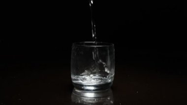 Koyu arkaplanda bardağa sıvı dökülüyor.