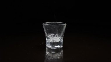 Koyu arkaplanda bardağa sıvı dökülüyor.