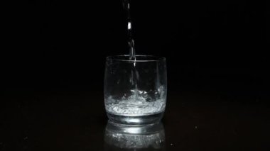Koyu arkaplanda bardağa sıvı dökülüyor.
