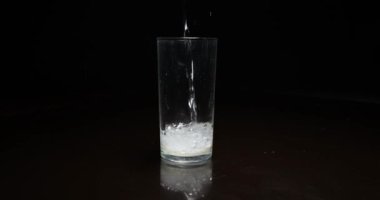 Koyu arkaplanda bardağa sıvı dökülüyor.