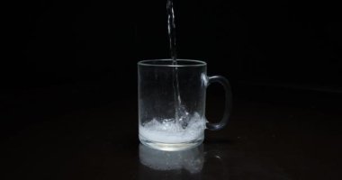 Koyu arkaplandaki şeffaf kupaya sıvı dökülüyor