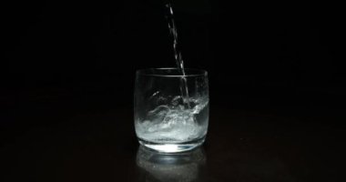 Koyu arkaplanda bardağa sıvı dökülüyor.