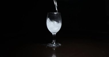 Koyu arkaplanda buzla bardağa alkol dökmek.