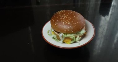 Siyah bir masada beyaz bir tabakla hamburger.
