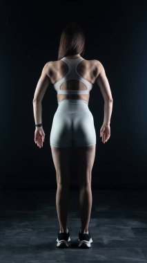 Atletik kadın siyah arka planda dambıllarla egzersiz yapıyor.