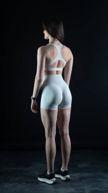 Beyaz takım elbiseli genç bayan atlet gri arka planda duruyor.