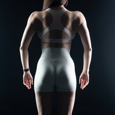 Spor kıyafetli genç bayan sporcunun arkadan görünüşü kollarını kavuşturup spor kulübündeki karanlık arka planda izole bir şekilde poz vermesi.