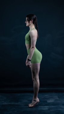 Spor kıyafetlerinde spor modelliği koyu arka planda poz vermek, stüdyo çekimi.