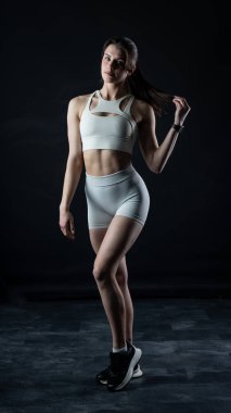 Karanlık bir stüdyoda dambılı olan genç bir kadın. fitness, vücut geliştirme, spor konsepti.