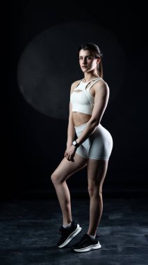 Dambıllarla poz veren genç atletik kadın. Stüdyo. koyu arkaplan.