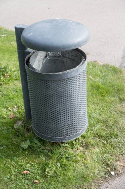 Temiz çevre ve kamusal alanlar kavramı olarak parkın çimenli yüzeyine kapaklı büyük metal çöp tenekesini kapat