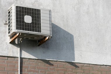Yazın klima ve modası geçmiş teknolojiler için konsept olarak klima kompresörünün dışına monte edilmiş, kısmen çatırdayan güneşli ev cephesi duvarı.