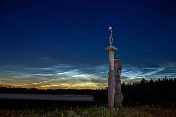 Noctilucent clouds in the fields of the Lithuanian countryside with sculptures on the ''M.K. Ciurlionis road'' near the village of Perloja