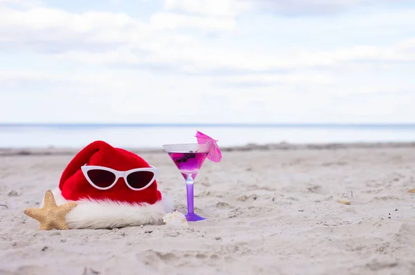 Christmas vacation at sea. Happy New Year holidays. Santa hat, starfish, sunglasses,coctail on sandy beach.Christmas card and advent calendar concept. Travel ticket sale concept for christmas holidays