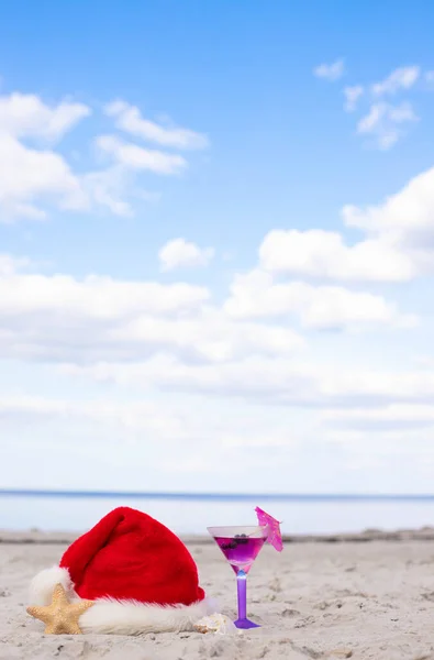 Christmas vacation at sea. Santa hat, starfish, coctail on sandy beach.Christmas card and advent calendar concept. Travel ticket sale concept for christmas holidays.Copy space.Close up.Vertical photo