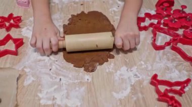 Çocuk zencefilli kurabiye hamuru ve kurabiye kesicilerden Noel kurabiyesi yapıyor. Çocuk oklavalı hamuru yuvarlıyor. Yüksek kaliteli fotoğraf..