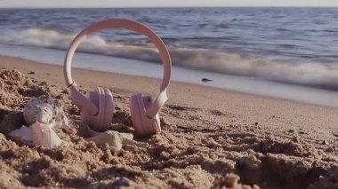 Yaz müziği arka planı pembe kablosuz kulaklıklar, deniz yıldızı ve deniz kabukları bir yaz gününde plajda uzanıyor. Yüksek kaliteli FullHD görüntüler