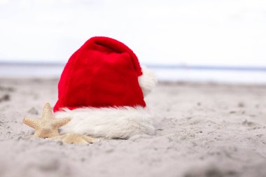 Noel arkaplanı. Noel Baba şapkası ve deniz yıldızı kumlu sahilde. Noel kartı ve yeni takvim konsepti. Noel tatilleri için bilet satışı konsepti. Kopya yer. Yüksek kalite fotoğraf.