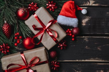 En üstteki fotoğrafta noel kutuları, kırmızı noel ağacı oyuncakları, Noel Baba şapkası ve ahşap arka planda ladin dalları var. Metin için alanı olan Xmas arkaplanı. Kopyalama alanı.