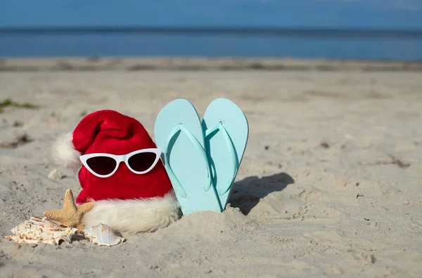 海でのクリスマス休暇 サンタクロースの帽子 ヒトデ 砂浜のビーチスリッパ クリスマスカードとアドベンチャーカレンダーのコンセプト クリスマス休暇の旅行チケット販売のコンセプト スペースをコピーします 閉じる — ストック写真