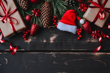 En üstteki fotoğrafta noel kutuları, kırmızı noel ağacı oyuncakları, Noel Baba şapkası ve ahşap arka planda ladin dalları var. Metin için alanı olan Xmas arkaplanı. Kopyalama alanı.