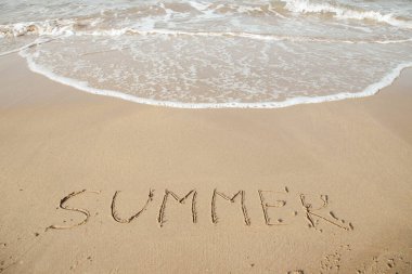 Summer 2023 lettering on the beach with wave and clear blue sea. Letters Summer 2023 on the sea shore, message handwritten in the golden sand on beautiful beach background. Summer Holidays 2023