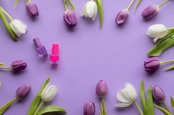 Nail polish and spring fresh tulips on violet background .Copy space.Top view photo.
