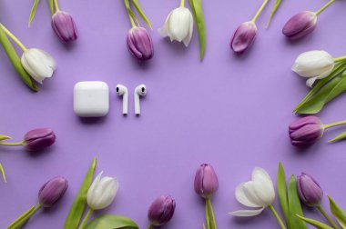 Wireless headphones pods and Spring tulips on violet background.Top view photo.Copy space.
