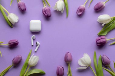 Wireless headphones pods and Spring tulips on violet background.Top view photo.Copy space.
