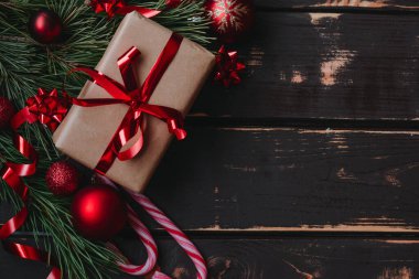 En üstteki fotoğrafta noel hediyesi kutusu, kırmızı noel ağacı oyuncakları, lolipoplar ve ladin brançı tahta zeminde. Boşluğu kopyala..