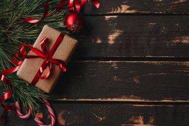 En üstteki fotoğrafta noel hediyesi kutusu, kırmızı noel ağacı oyuncakları, lolipoplar ve ladin brançı tahta zeminde. Boşluğu kopyala..
