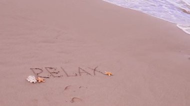 Yazı, plajdaki beyaz kumda rahatla, metnin yanındaki deniz yıldızı ve deniz kabukları, dalgalar. Tatil ve yaz tatili konsepti. Yüksek kaliteli FullHD görüntüler