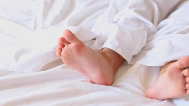 Μικρά Κοριτσίστικα Πόδια Ξεπροβάλλουν Κάτω Από Μια Λευκή Κουβέρτα Πρωί — Αρχείο Βίντεο