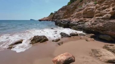 Zaman çizelgesi, Benidorm, İspanya 'da insansız bir sahile yakın. Körfez, sahil kıyısının arkasında yer alıyor. Dalgalar plaj sahili görüntülerinde kayalara çarpıyor.