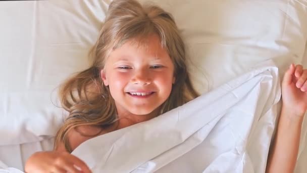 Ένα Γοητευτικό Χαρούμενο Κοριτσάκι Μακριά Μαλλιά Βρίσκεται Ένα Λευκό Κρεβάτι — Αρχείο Βίντεο