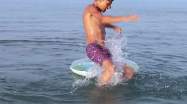 Yavaş hareket eden genç, deniz suyunda renkli şişme yüzme kucağına atlıyor. Yaz tatilindeki genç, suda eğleniyor. Aile tatilleri ve tatil konsepti. Yüksek kaliteli FullHD görüntüleri.