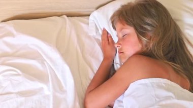 Uzun saçlı küçük bir kız sabahın köründe beyaz bir yastığın üzerinde huzurlu bir yatakta uyuyor. Ağır çekim üst görünüm klibini kapat. Aile, çocukluk veya diğer projeler için mükemmel.