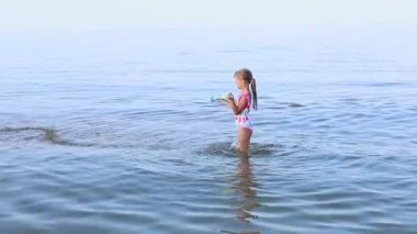  Avrupa görünümlü 7 yaşındaki mutlu kız denizlerde su tabancasıyla oynuyor. Aile yaz mesleği kavramı. Yüksek kaliteli FullHD görüntüler
