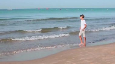 Beyaz tişörtlü yakışıklı çocuk yaz tatilinin tadını çıkarıyor. Aile tatilleri, tatiller, seyahatler, seyahat konsepti. Düşük hareketli kenar açı klibi. Yüksek kaliteli FullHD.