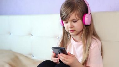 Kulaklık takmış, müzik dinleyen, akıllı telefon kullanarak dans eden, evdeki bir yatakta oturan, ağır çekimde kapanış yapan sevimli, genç kız. Yüksek kalite 4k görüntü