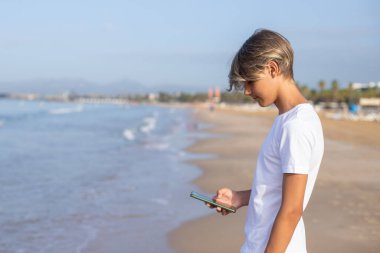 Yaz tatillerinde plajda akıllı telefon kullanan beyaz tişörtlü yakışıklı delikanlıyı kapat. İspanya 'da seyahat, tatil, tatil, özgürlük kavramı.. 